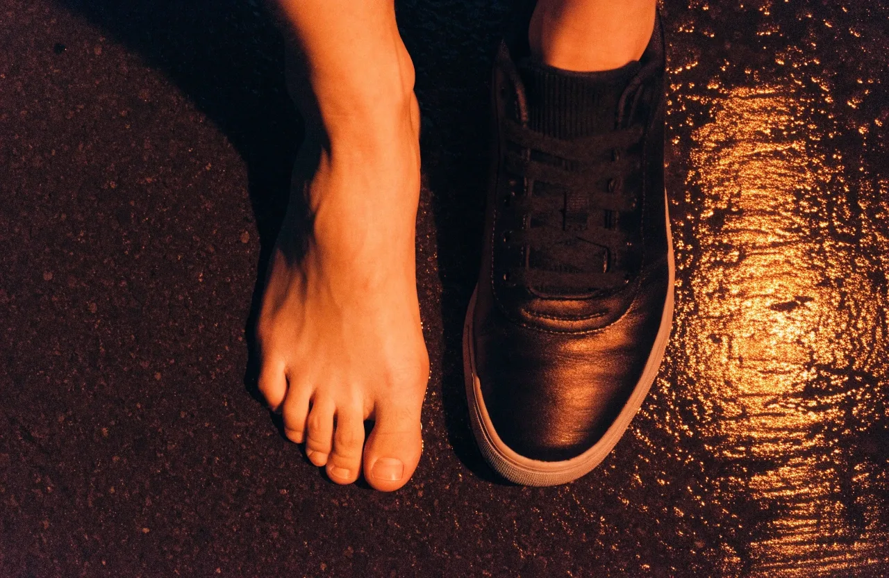 Pied posé à côté d'une sneaker sans marque sur un sol mouillé, vu de dessus