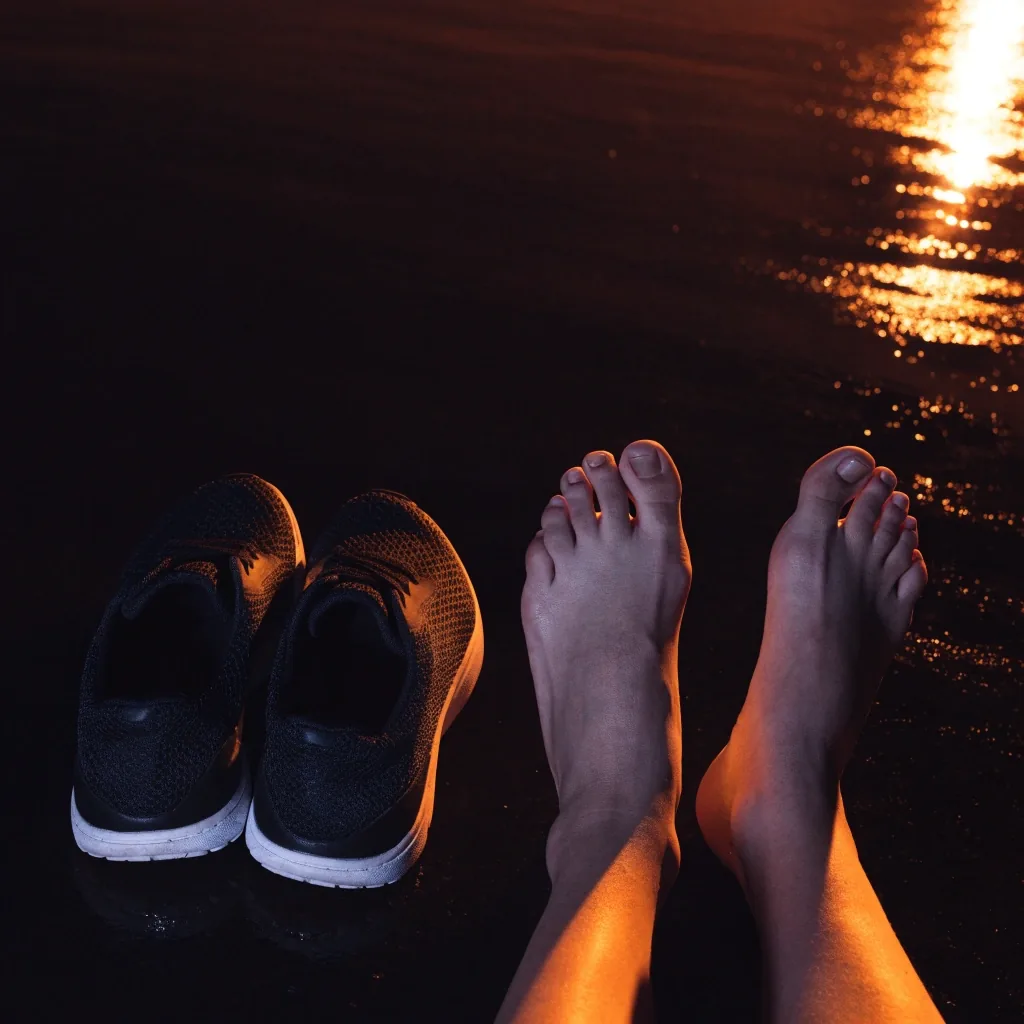 Pieds nus posés à côté d'une paire de chaussures de running sur un sol sombre mouillé