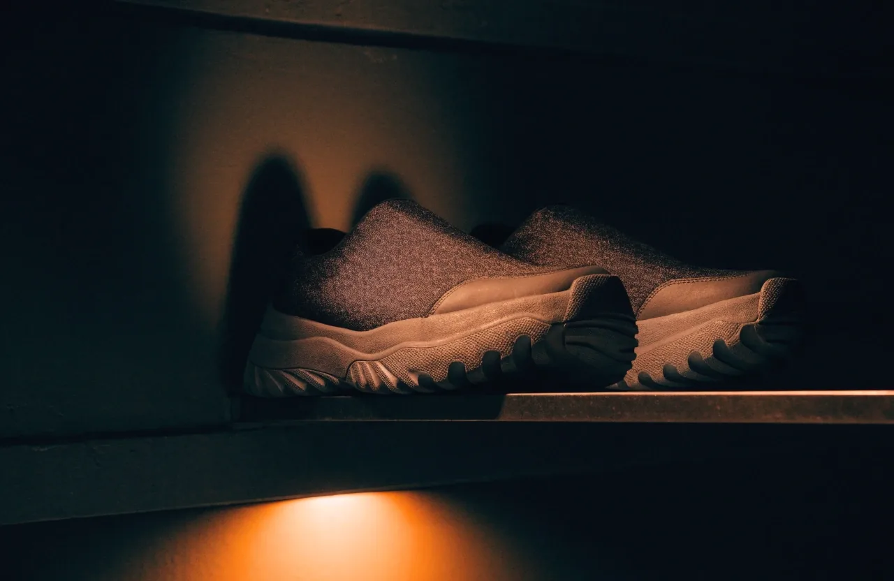 Paire de sneakers urbaines basses posée sur une étagère murale fine, vue de profil sous une lumière de rue orangée
